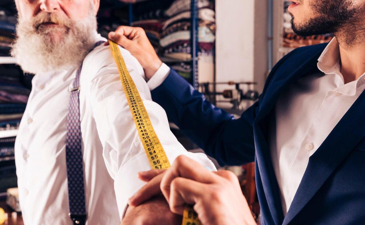 Close-up of male tailor taking measurement of senior man's sleeves