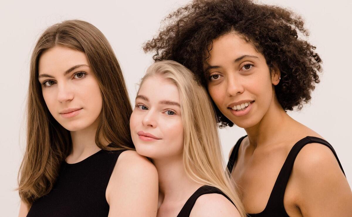 Closeup of young women of different nationalities in black tops looking at camera on white background