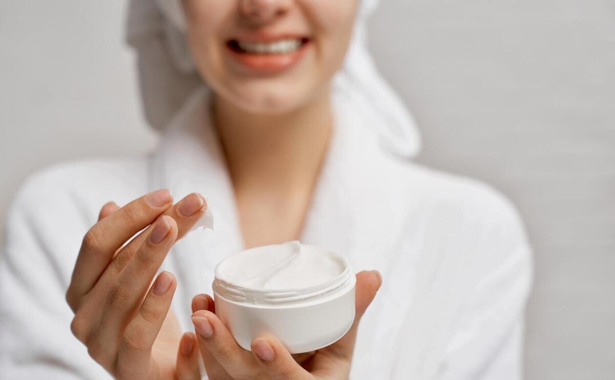 Young woman close up holding moisturizer and demonstrates