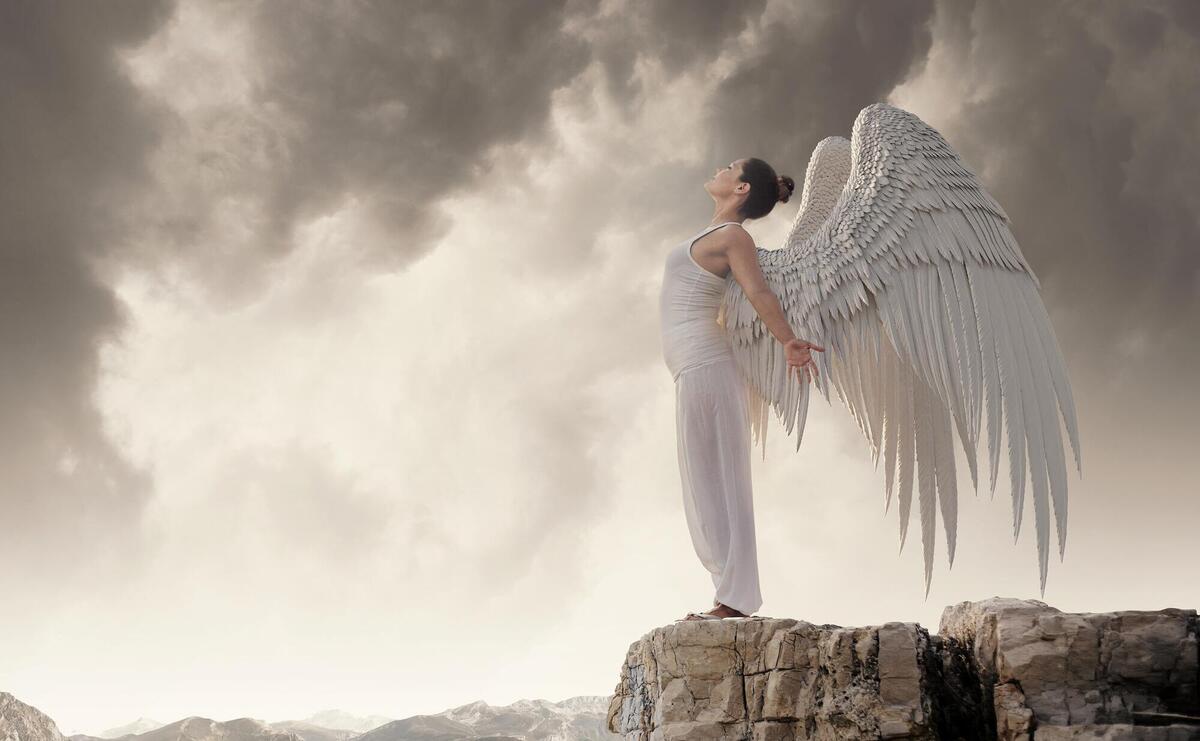 Woman dressed in white clothes with wings outdoors.