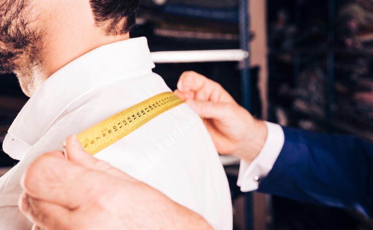 Fashion designer taking measurement of his customer's back with yellow measuring tape