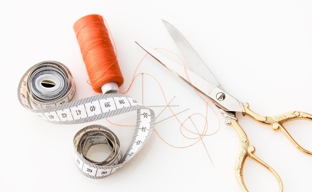 A measuring tape, golden scissors, and a needle with thread.