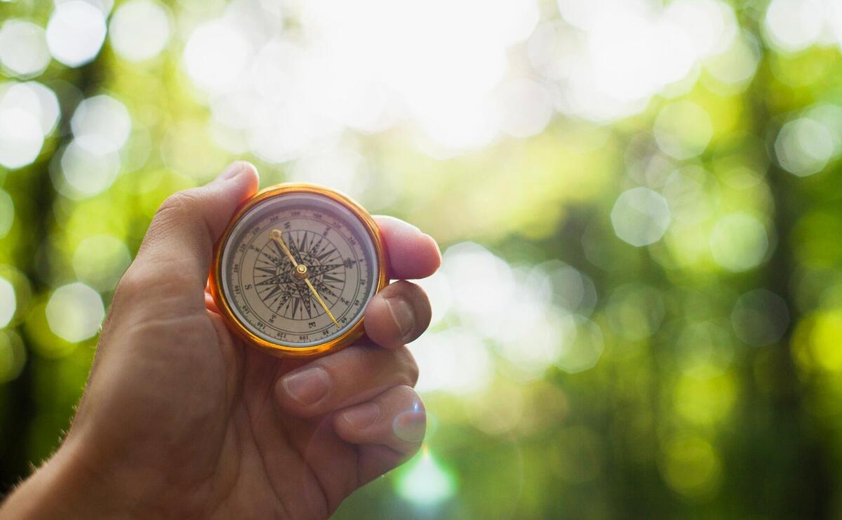 Hand holding a compass with blurred background.