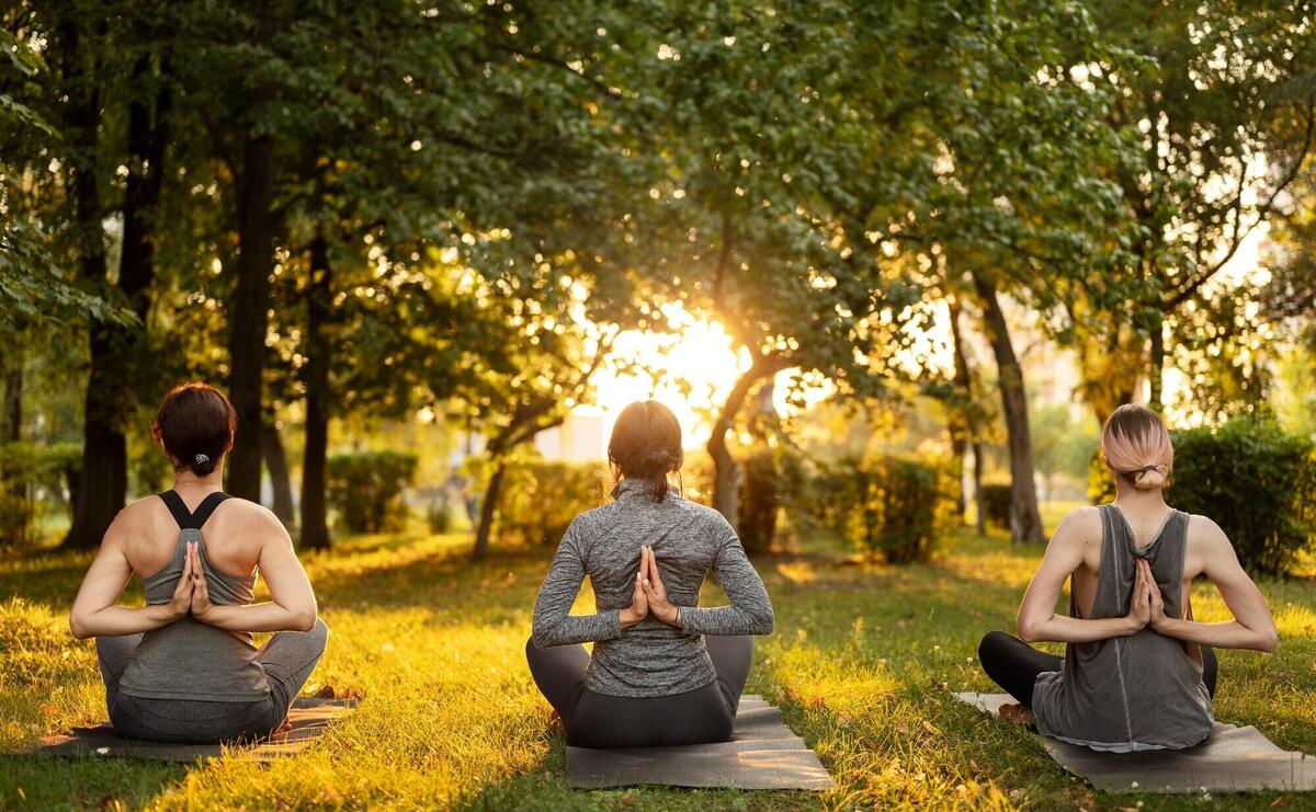 Three individuals meditating in a sunlit park, finding peace.