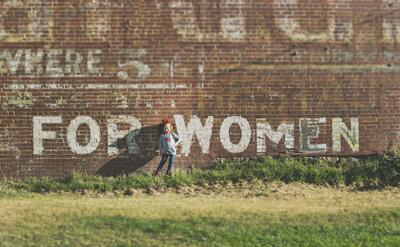 Little girl standing in a brick wall, with "For Woman" graffiti on it.