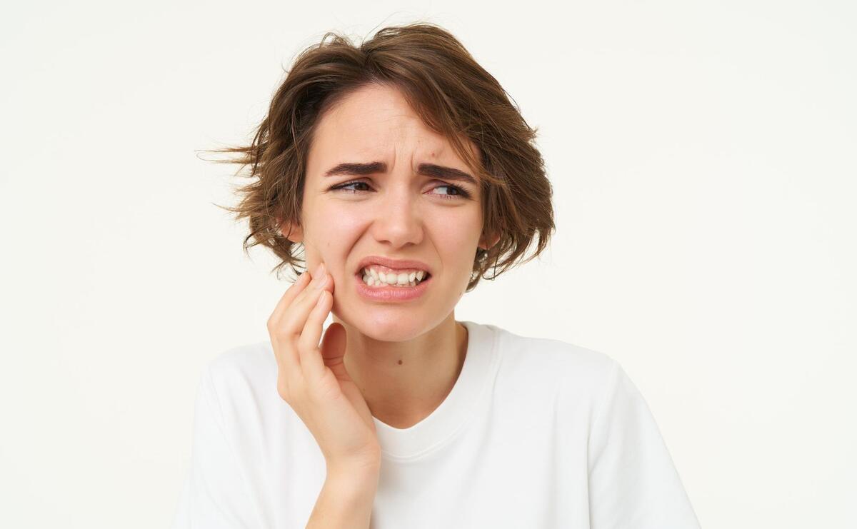 Woman has a toothache touches her teeth and frowns from painful discomfort stands over.