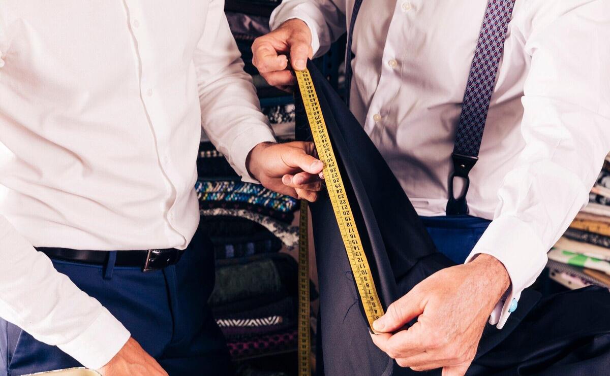 Customer and senior male tailor measuring the fabric with yellow measure table
