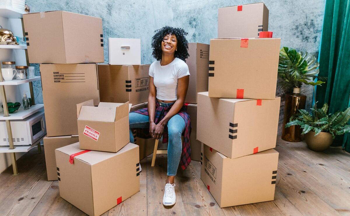Photograph of a Woman in a White Shirt Sitting Beside Cardboard Boxes