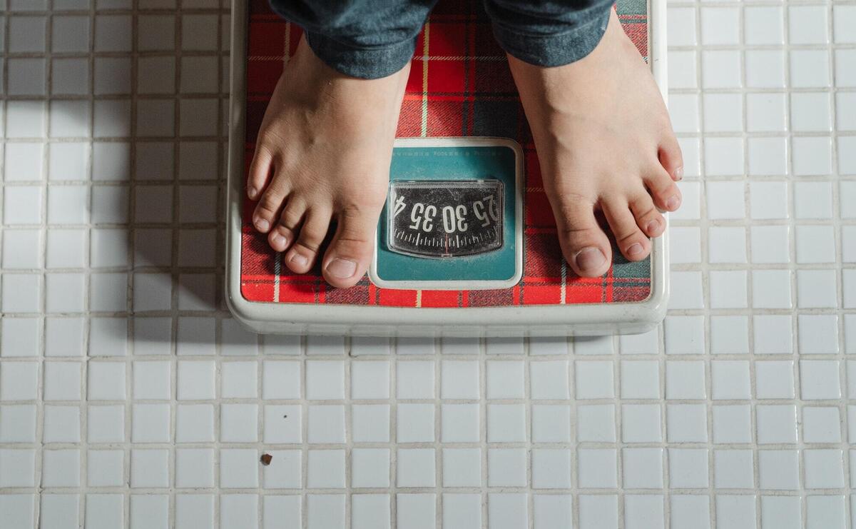 From above crop anonymous barefoot child in jeans standing on weigh scales on tiled floor of bathroom