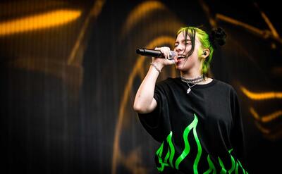 Billie Eilish singing on stage with green hair