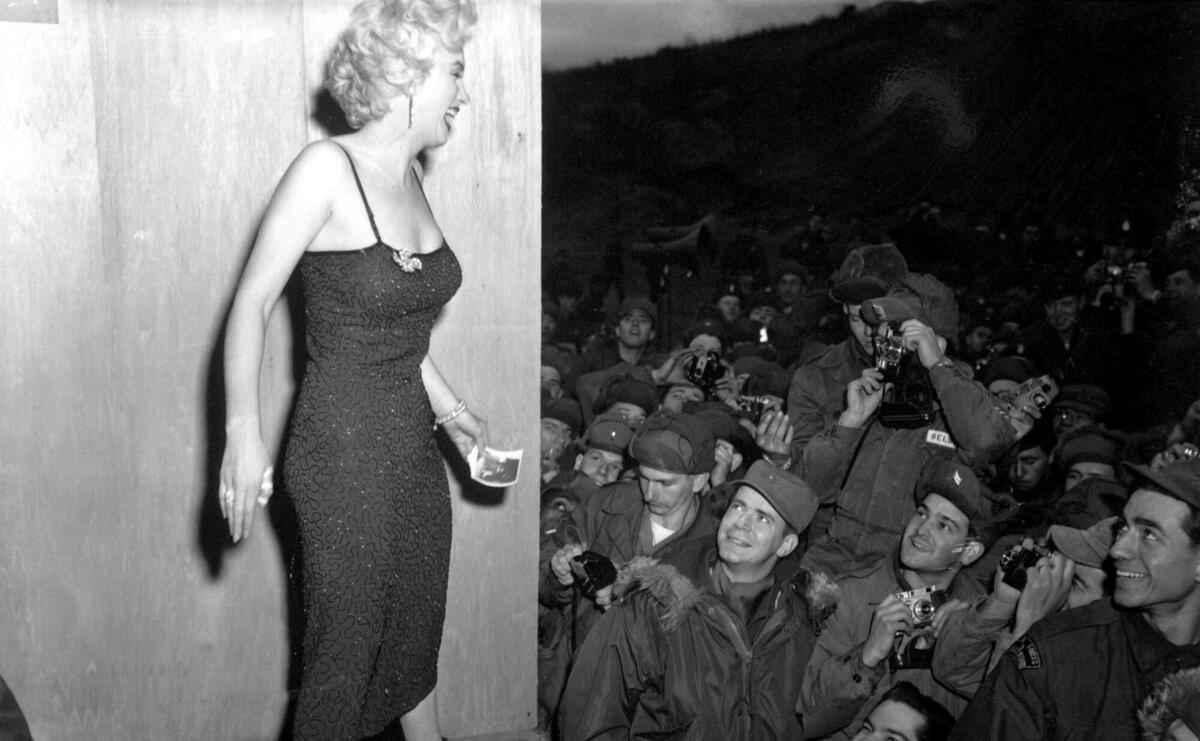 Marilyn Monroe smiling among a crowd of soldiers.