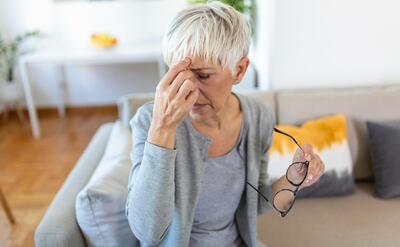 Senior woman in glasses rubs her eyes suffering from tired eyes ocular diseases.