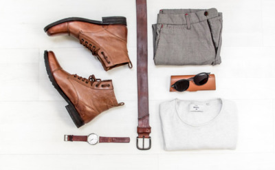 A pair of brown leather boots, beige chinos, brown leather belt, round gold-colored watch, and creamy top