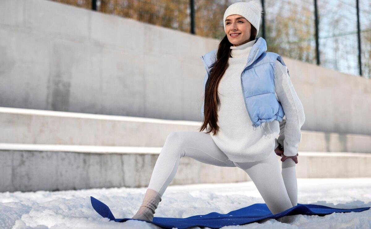 Young woman practicing yoga outdoors during winter in warm clothes