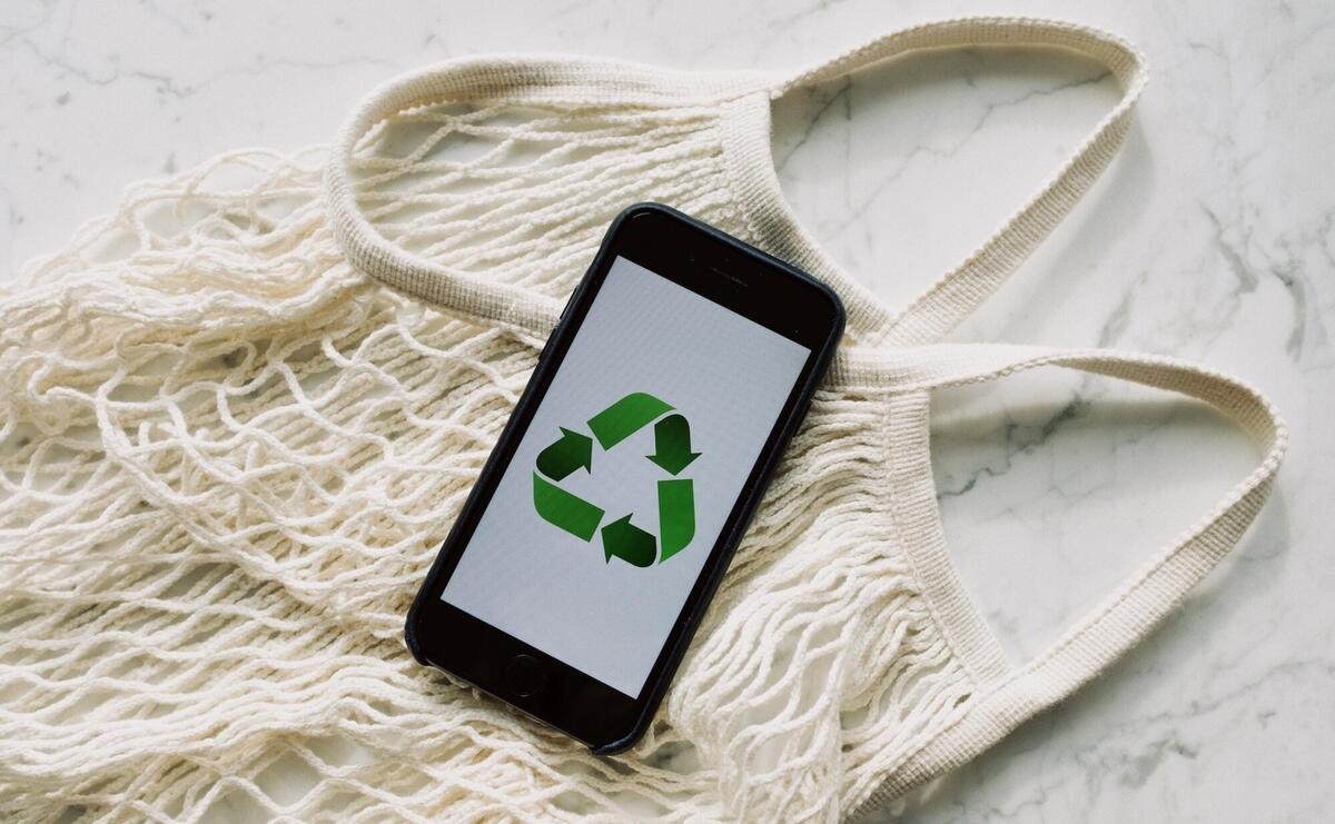 Smartphone with recycling sign on screen placed on white mesh bag