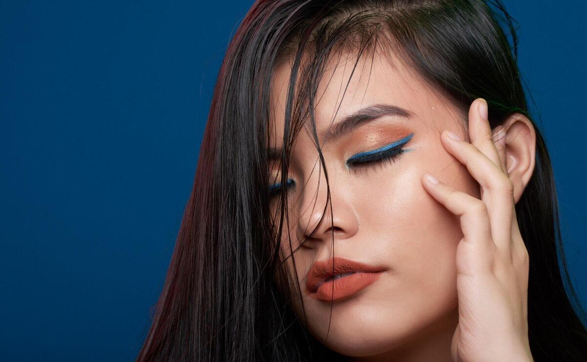 Closeup of asian woman with full makeup posing in studio with closed eyes and fingers on temple